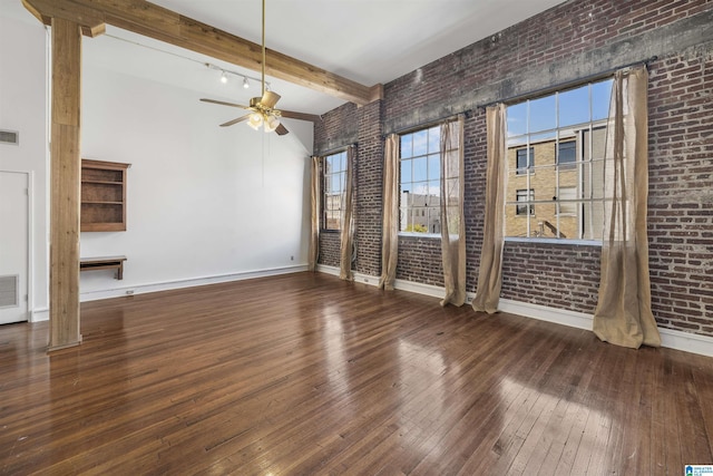 unfurnished room with baseboards, beam ceiling, hardwood / wood-style flooring, and brick wall