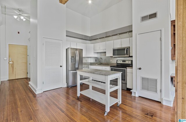 kitchen featuring stainless steel appliances, white cabinets, a towering ceiling, hardwood / wood-style floors, and ceiling fan