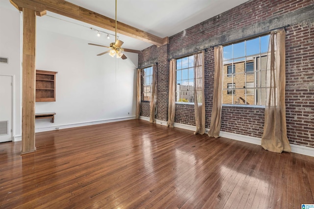 unfurnished living room with a towering ceiling, hardwood / wood-style floors, beamed ceiling, ceiling fan, and brick wall