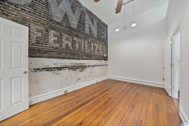 empty room with a towering ceiling, brick wall, hardwood / wood-style flooring, and ceiling fan