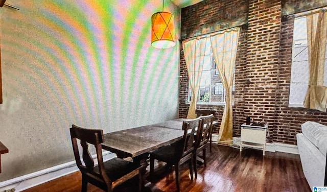 dining area with brick wall and dark hardwood / wood-style flooring