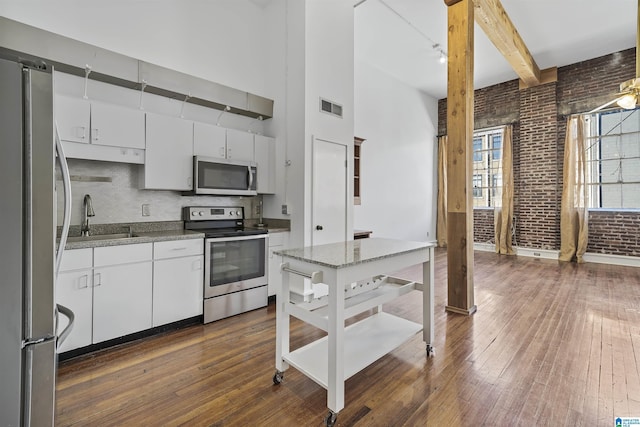 kitchen with brick wall, stainless steel appliances, a sink, visible vents, and a towering ceiling