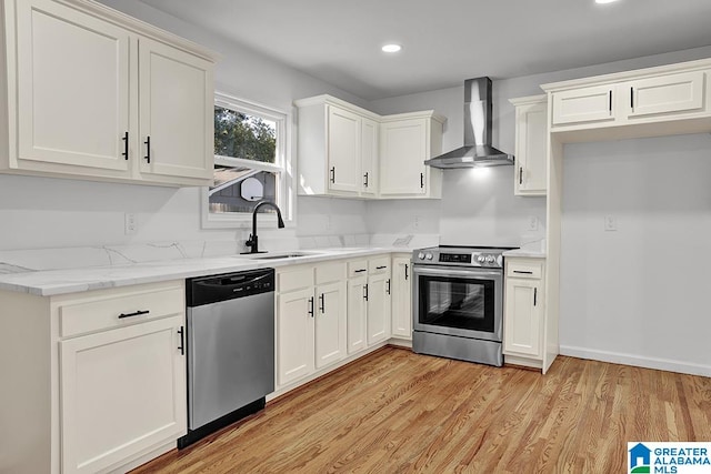 kitchen featuring wall chimney range hood, sink, white cabinets, appliances with stainless steel finishes, and light hardwood / wood-style floors