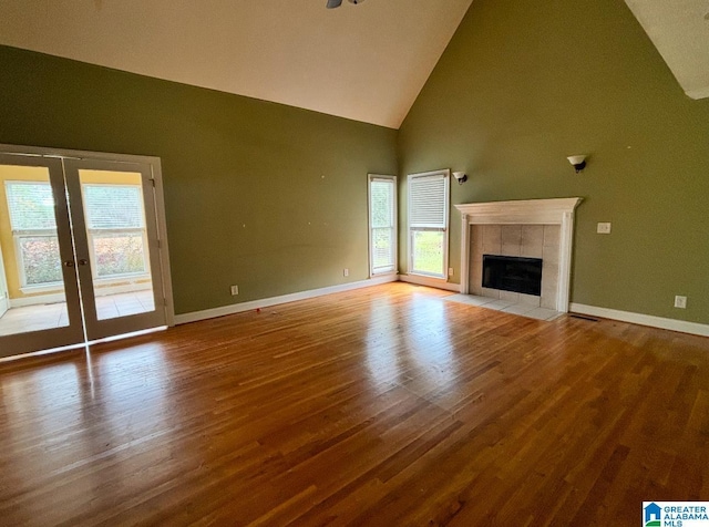 unfurnished living room with french doors, high vaulted ceiling, a fireplace, and wood-type flooring