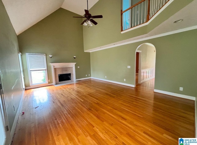 unfurnished living room with hardwood / wood-style floors, a fireplace, ceiling fan, high vaulted ceiling, and crown molding