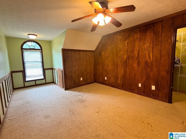 bonus room featuring a textured ceiling, light carpet, wooden walls, vaulted ceiling, and ceiling fan