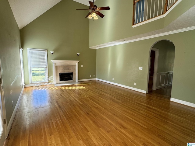 unfurnished living room with high vaulted ceiling, wood-type flooring, a tile fireplace, and ceiling fan