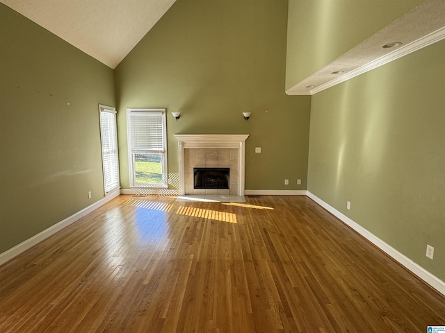 unfurnished living room with high vaulted ceiling, hardwood / wood-style floors, and a tile fireplace