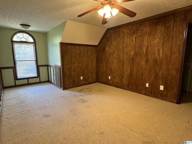 additional living space with wooden walls, a textured ceiling, and lofted ceiling