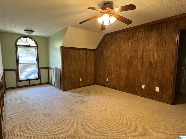 bonus room with light carpet, ceiling fan, a textured ceiling, wood walls, and lofted ceiling