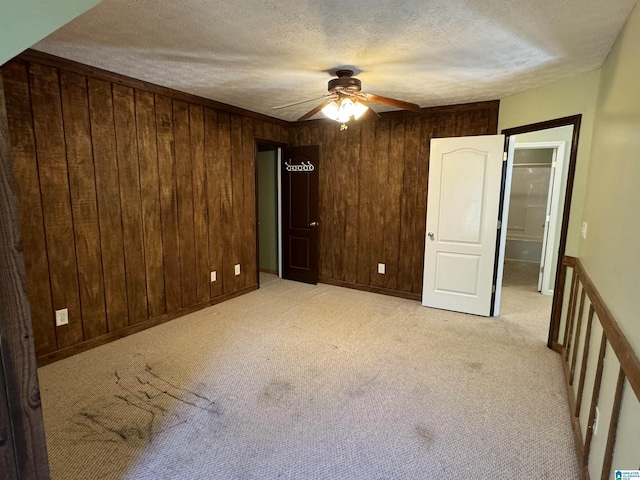 unfurnished bedroom with wood walls, light colored carpet, a textured ceiling, and ceiling fan