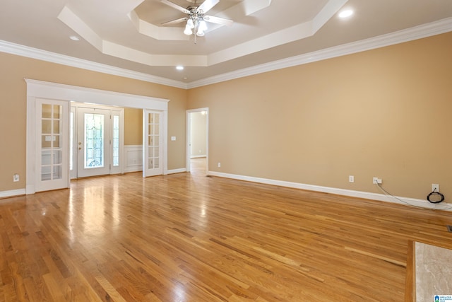 spare room with a tray ceiling, french doors, crown molding, and light wood-type flooring