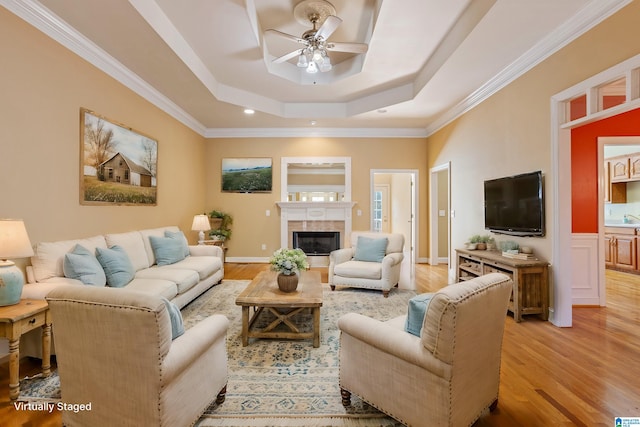 living room with ceiling fan, a raised ceiling, ornamental molding, and light hardwood / wood-style flooring