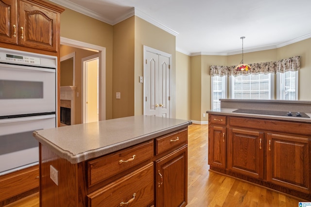 kitchen with a kitchen island, black electric stovetop, ornamental molding, light wood-type flooring, and white double oven