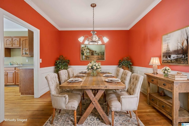 dining space with light hardwood / wood-style floors, a notable chandelier, ornamental molding, and sink