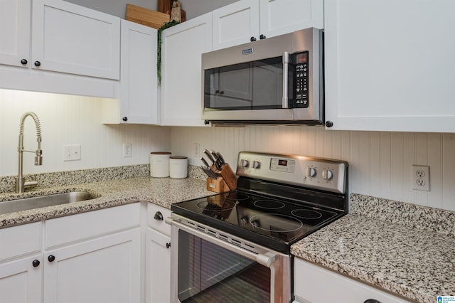 kitchen with appliances with stainless steel finishes, white cabinets, light stone countertops, and sink