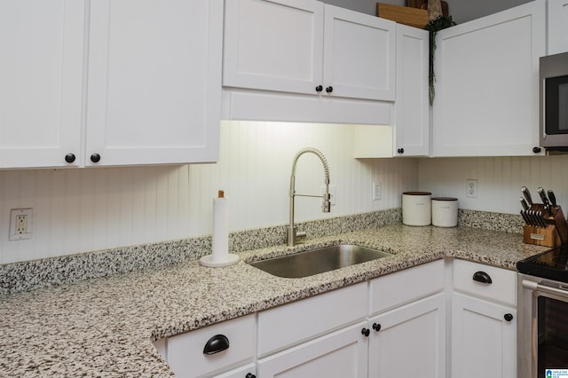 kitchen featuring appliances with stainless steel finishes, sink, white cabinets, and light stone counters