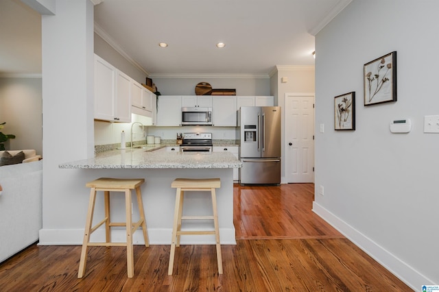 kitchen with kitchen peninsula, white cabinets, hardwood / wood-style floors, appliances with stainless steel finishes, and crown molding