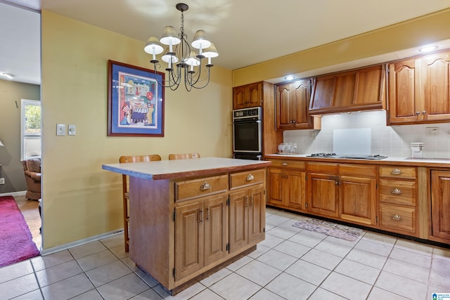 kitchen with decorative backsplash, hanging light fixtures, a center island, light tile patterned floors, and stainless steel gas stovetop