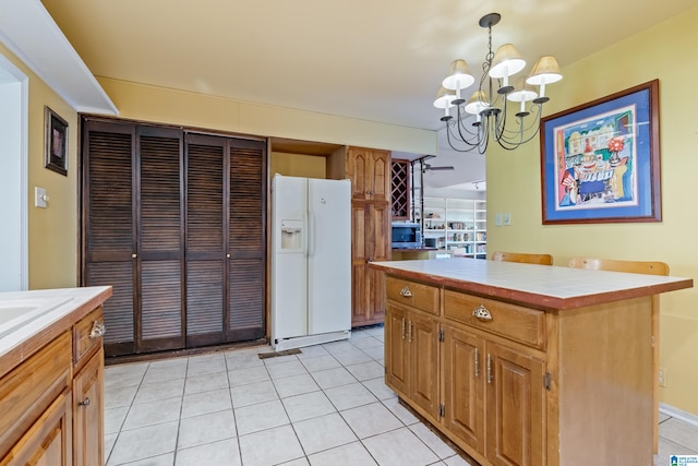 kitchen featuring a kitchen island, white refrigerator with ice dispenser, hanging light fixtures, light tile patterned floors, and an inviting chandelier