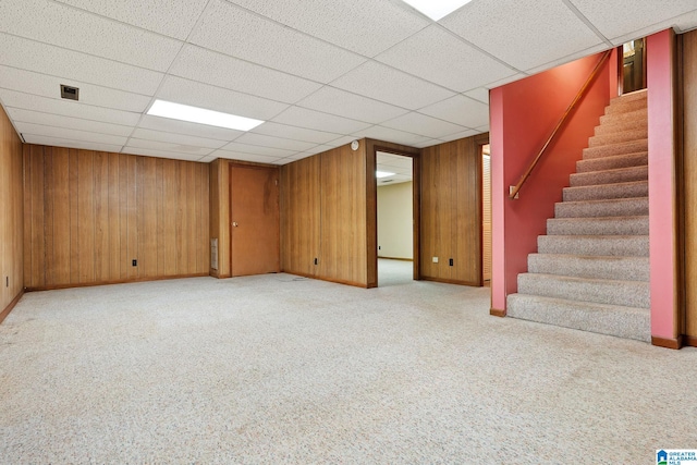 basement with wood walls, light colored carpet, and a paneled ceiling