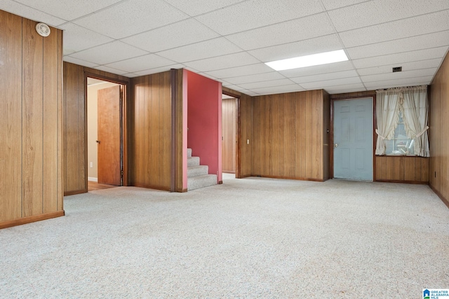 basement featuring light carpet, wood walls, and a paneled ceiling