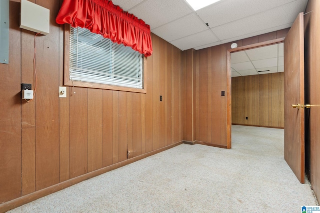 empty room with light carpet, a paneled ceiling, and wood walls