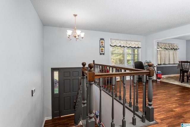 stairway featuring a textured ceiling, wood-type flooring, and an inviting chandelier