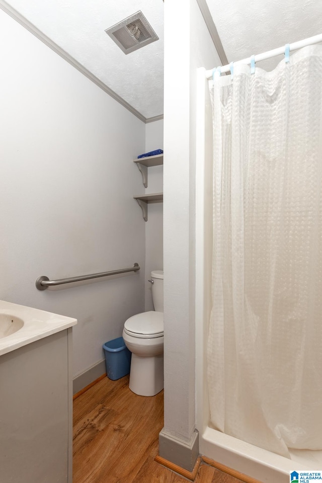 bathroom featuring walk in shower, hardwood / wood-style flooring, toilet, vanity, and crown molding