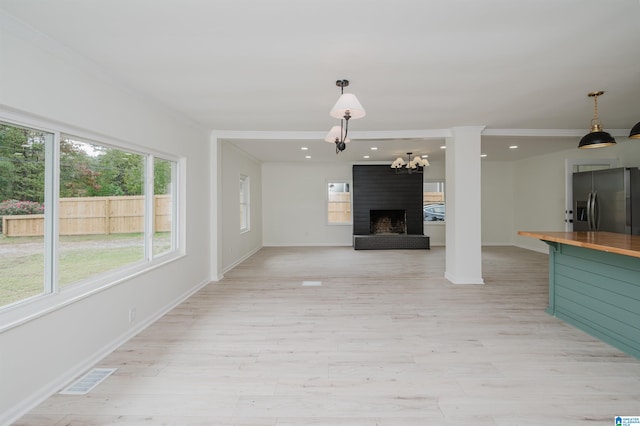 unfurnished living room with ornamental molding, light wood-type flooring, a fireplace, and an inviting chandelier