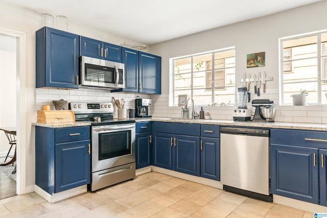 kitchen with decorative backsplash, appliances with stainless steel finishes, light stone countertops, sink, and blue cabinets