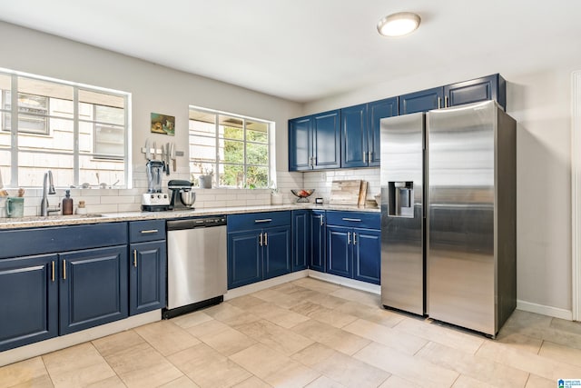 kitchen featuring stainless steel appliances, sink, light stone countertops, blue cabinetry, and tasteful backsplash