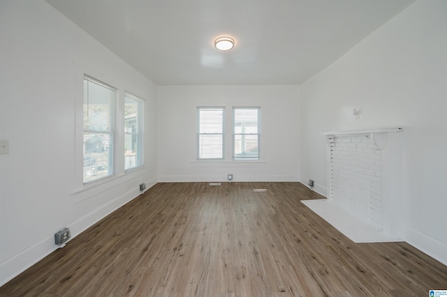 empty room featuring wood-type flooring and a brick fireplace