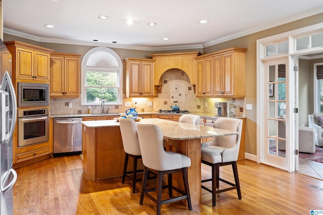 kitchen featuring tasteful backsplash, light stone counters, appliances with stainless steel finishes, light hardwood / wood-style floors, and a center island