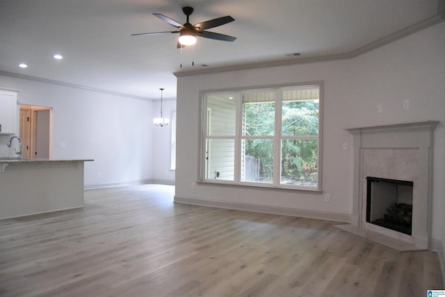 unfurnished living room with crown molding, a fireplace with flush hearth, light wood-type flooring, ceiling fan with notable chandelier, and a sink