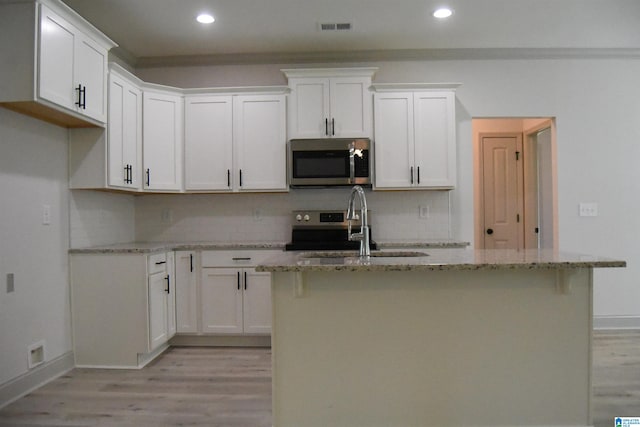 kitchen featuring light stone countertops, visible vents, light wood finished floors, a sink, and stainless steel microwave