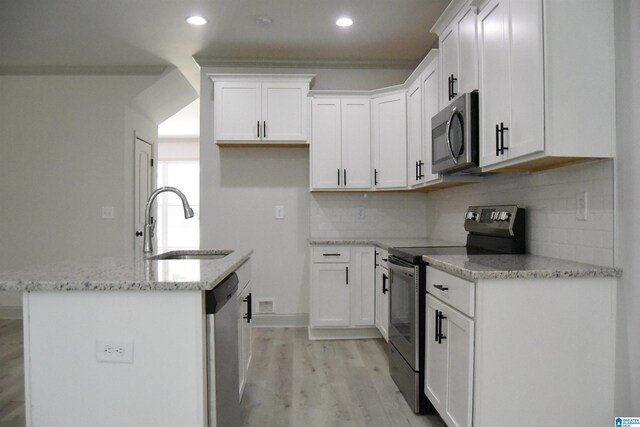 kitchen with a center island with sink, a sink, white cabinets, light wood-style floors, and appliances with stainless steel finishes