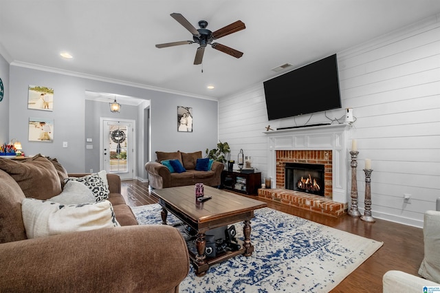 living room featuring a brick fireplace, ceiling fan, wooden walls, dark wood-type flooring, and crown molding