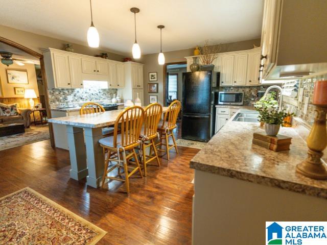 kitchen featuring dark hardwood / wood-style floors, decorative light fixtures, black refrigerator, and ceiling fan