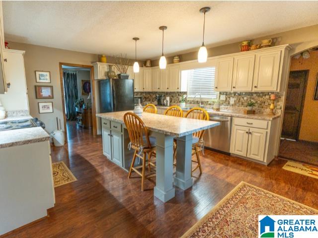 kitchen featuring a kitchen bar, a kitchen island, hanging light fixtures, stainless steel dishwasher, and black refrigerator