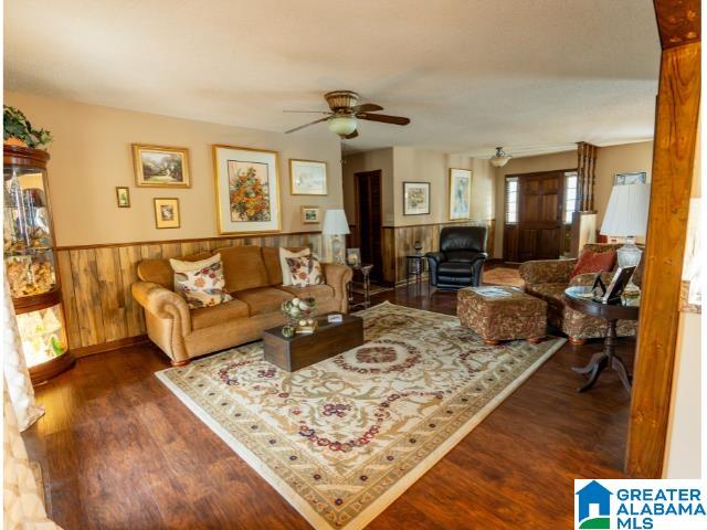 living room featuring wooden walls, dark wood-type flooring, and ceiling fan