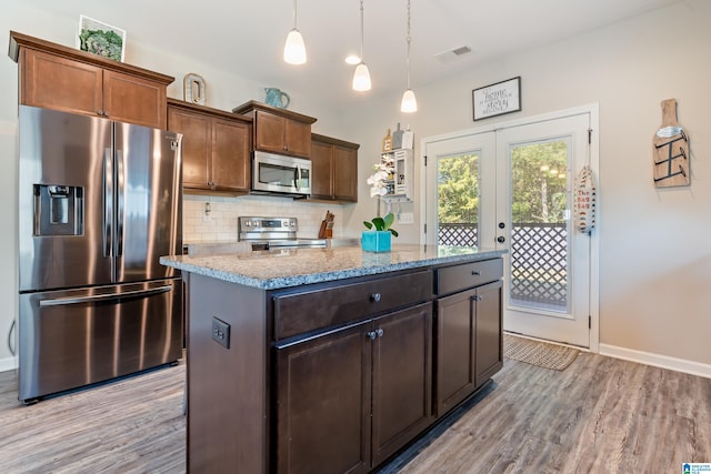 kitchen with light stone counters, appliances with stainless steel finishes, light wood-type flooring, pendant lighting, and a center island