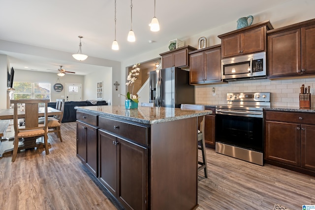 kitchen with dark brown cabinets, a kitchen island, appliances with stainless steel finishes, hardwood / wood-style flooring, and pendant lighting