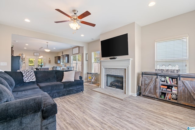 living room with a brick fireplace, light wood-type flooring, and ceiling fan