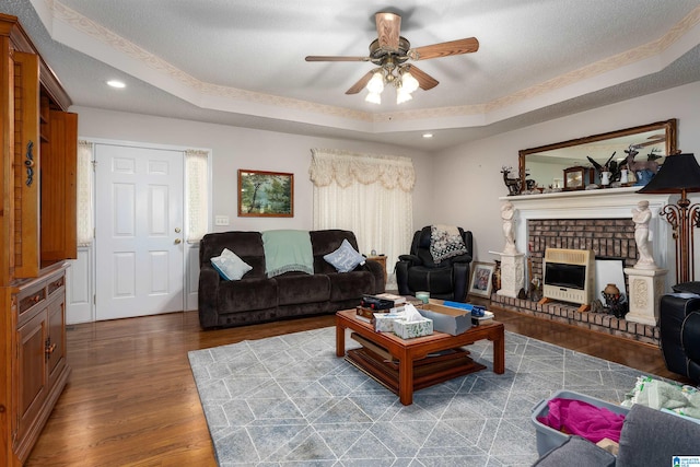 living room featuring ceiling fan, a raised ceiling, wood-type flooring, and a fireplace