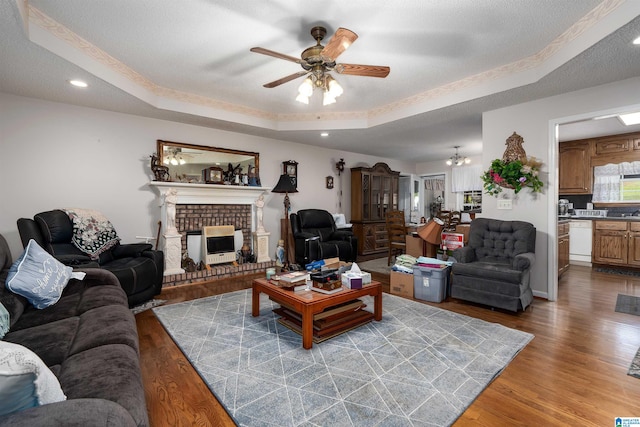 living room featuring ceiling fan, a textured ceiling, wood-type flooring, a tray ceiling, and a brick fireplace