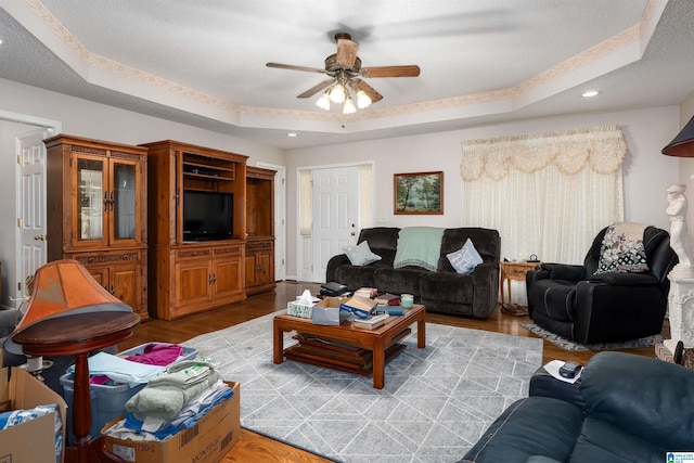 living room featuring ceiling fan, light wood-type flooring, and a raised ceiling