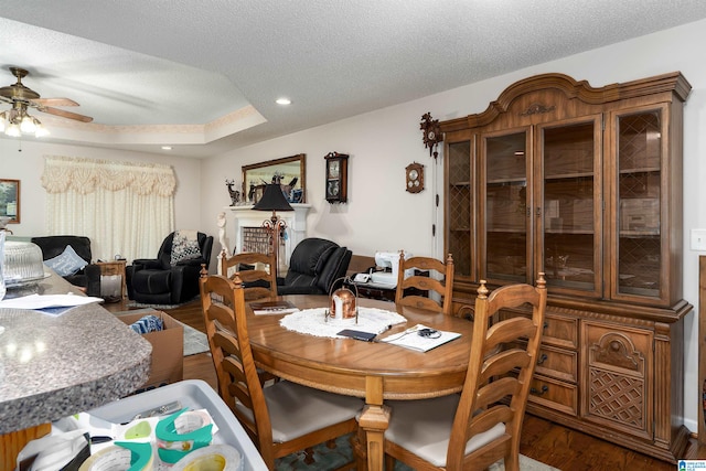 dining room with ceiling fan, hardwood / wood-style flooring, a textured ceiling, and a brick fireplace