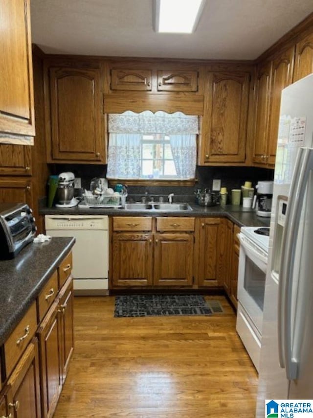 kitchen featuring sink, light wood-type flooring, white appliances, and dark stone counters