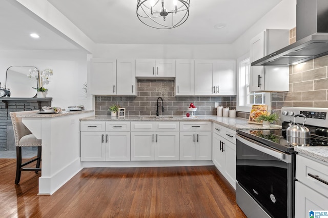 kitchen featuring dark hardwood / wood-style floors, wall chimney exhaust hood, stainless steel range with electric stovetop, sink, and white cabinets